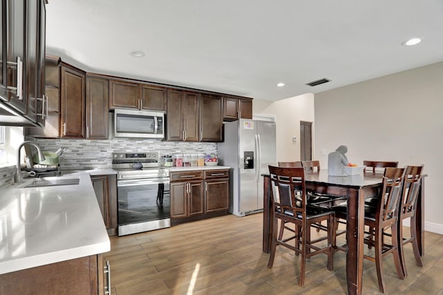 kitchen with appliances with stainless steel finishes, hardwood / wood-style flooring, sink, dark brown cabinets, and backsplash