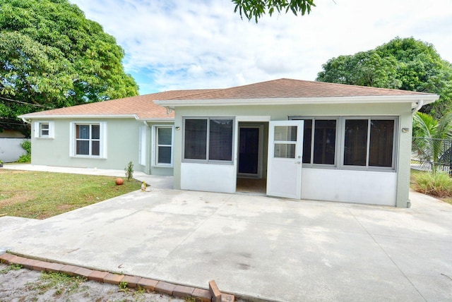 back of property with stucco siding, a yard, roof with shingles, and fence