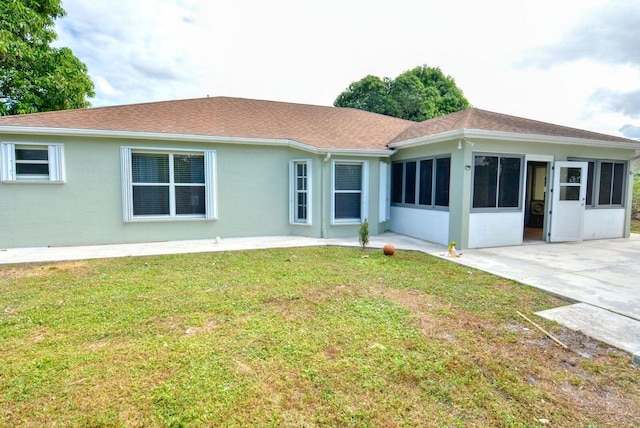 back of property with a yard, stucco siding, a shingled roof, and a patio