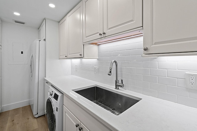 kitchen with sink, white fridge with ice dispenser, light wood-type flooring, white cabinetry, and washer / clothes dryer