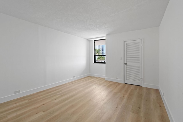 empty room with a textured ceiling and light hardwood / wood-style flooring