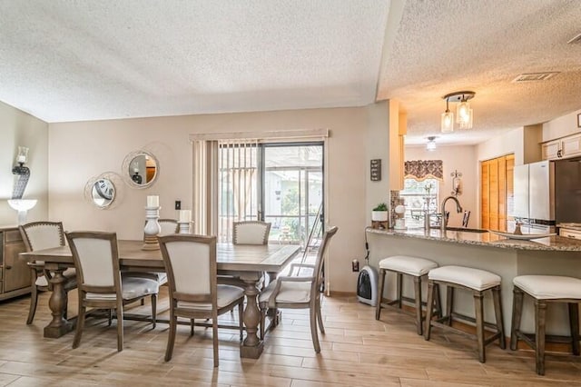 dining space featuring a textured ceiling, light hardwood / wood-style flooring, and sink