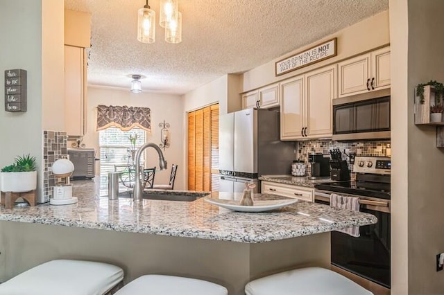 kitchen with cream cabinetry, a kitchen breakfast bar, stainless steel appliances, and hanging light fixtures