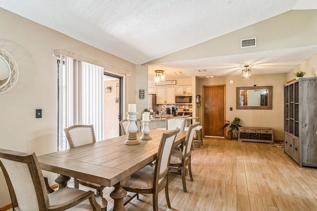 dining room with a textured ceiling, light hardwood / wood-style floors, and lofted ceiling