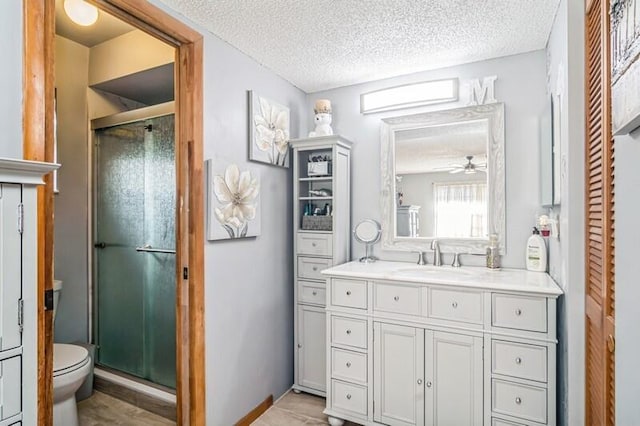 bathroom with a textured ceiling, vanity, ceiling fan, toilet, and a shower with shower door