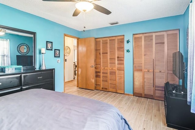 bedroom with a textured ceiling, ceiling fan, two closets, and light wood-type flooring