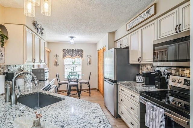 kitchen with appliances with stainless steel finishes, tasteful backsplash, sink, decorative light fixtures, and light hardwood / wood-style flooring