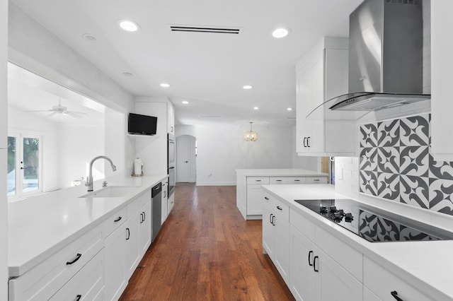 kitchen with appliances with stainless steel finishes, a peninsula, arched walkways, wall chimney exhaust hood, and a sink