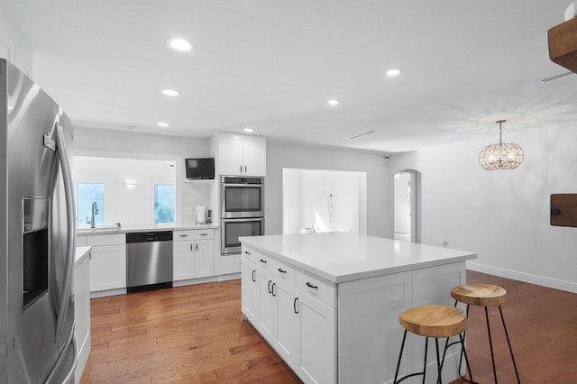 kitchen with a kitchen bar, a sink, arched walkways, light wood-style floors, and appliances with stainless steel finishes