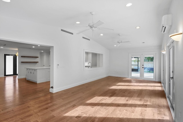 unfurnished living room with a wall unit AC, light wood-style flooring, recessed lighting, vaulted ceiling, and french doors