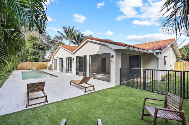 rear view of property featuring a sunroom, a fenced in pool, a patio, and a lawn