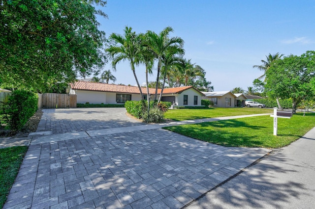 ranch-style house featuring fence, a tile roof, a front yard, stucco siding, and driveway