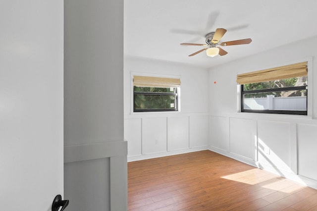 unfurnished room with a decorative wall, wainscoting, a ceiling fan, and wood finished floors