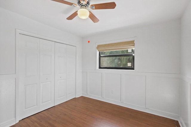 unfurnished bedroom featuring ceiling fan, a closet, wood finished floors, and wainscoting