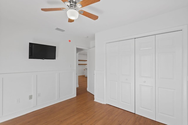 unfurnished bedroom featuring visible vents, wood finished floors, a closet, arched walkways, and a decorative wall