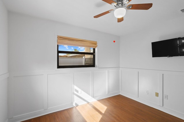 empty room featuring ceiling fan, a wainscoted wall, and wood finished floors