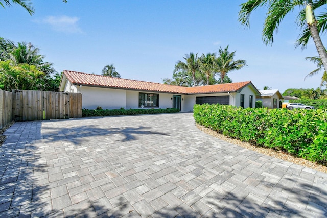 view of front of house with stucco siding, a tile roof, decorative driveway, fence, and an attached garage