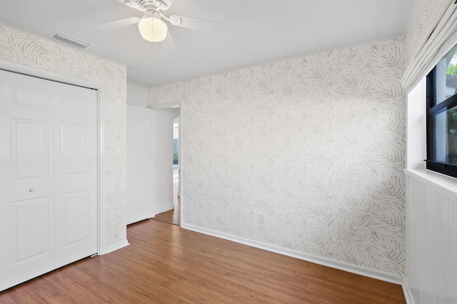 unfurnished bedroom featuring wallpapered walls, wood finished floors, visible vents, and baseboards