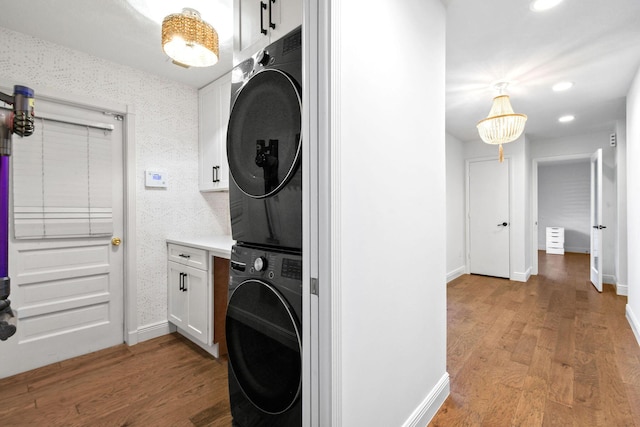 washroom with stacked washer / dryer, cabinet space, baseboards, and light wood finished floors