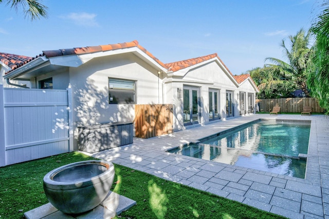 back of house featuring stucco siding, fence, french doors, a fenced in pool, and a tiled roof