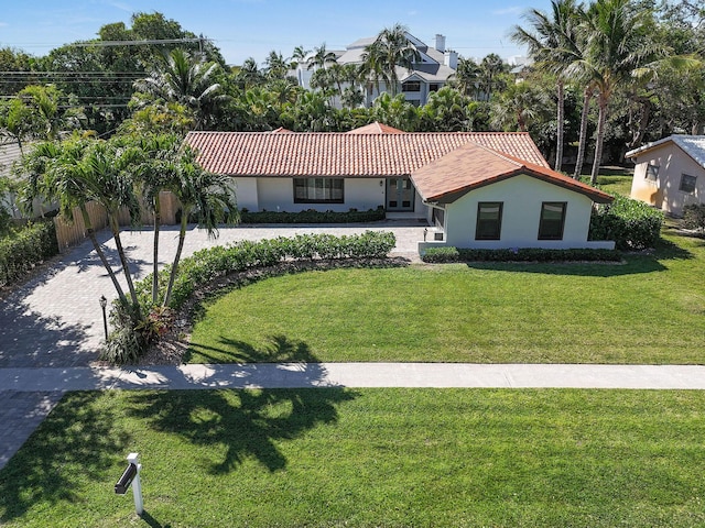 mediterranean / spanish home with stucco siding, driveway, a tile roof, and a front lawn