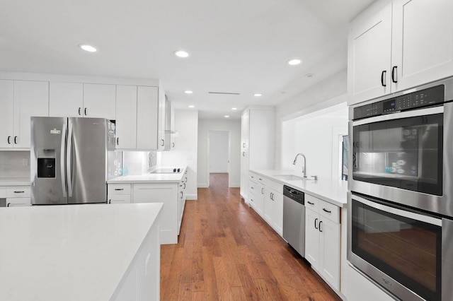 kitchen featuring a sink, wood finished floors, stainless steel appliances, light countertops, and decorative backsplash