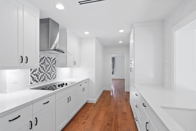 kitchen with black electric stovetop, wall chimney range hood, light countertops, decorative backsplash, and dark wood-style flooring