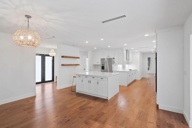 kitchen featuring white cabinets, light hardwood / wood-style floors, decorative light fixtures, a kitchen island, and stainless steel fridge with ice dispenser