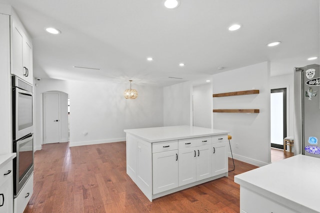 kitchen featuring white cabinetry, light countertops, wood finished floors, and arched walkways