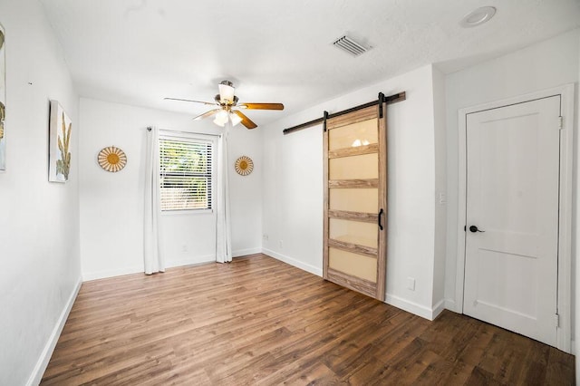 unfurnished room with hardwood / wood-style floors, a barn door, and ceiling fan