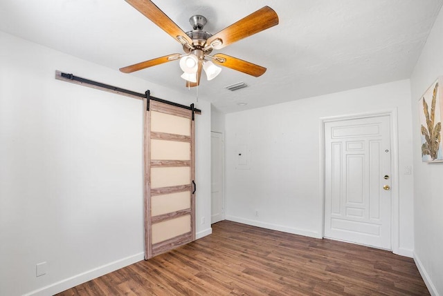 spare room with dark hardwood / wood-style floors, a barn door, and ceiling fan