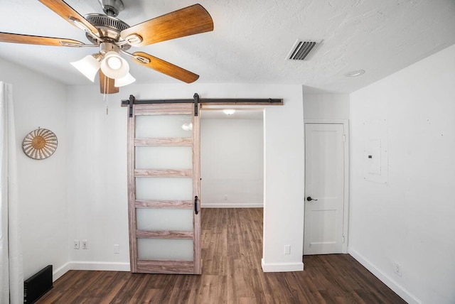 unfurnished bedroom featuring ceiling fan, a barn door, dark hardwood / wood-style flooring, and electric panel