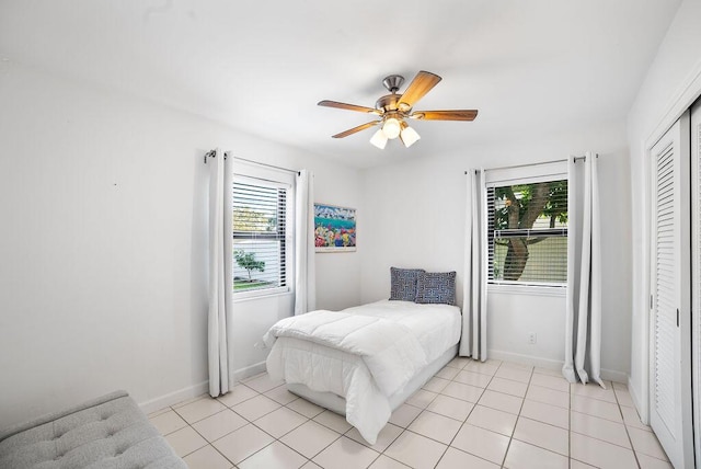 bedroom with multiple windows, ceiling fan, a closet, and light tile patterned flooring