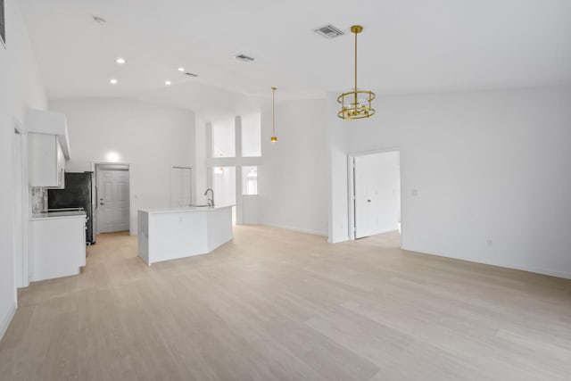 unfurnished living room with sink, high vaulted ceiling, light hardwood / wood-style floors, and a notable chandelier