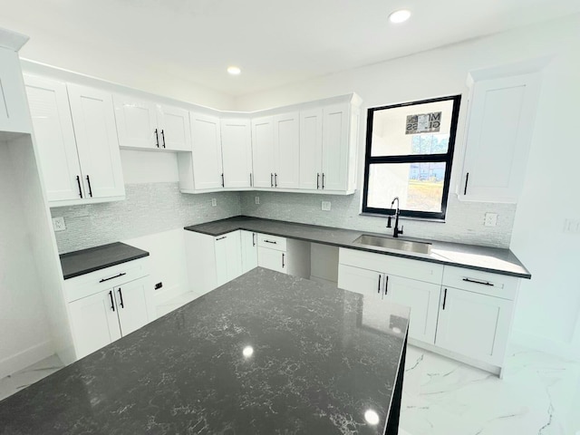 kitchen with decorative backsplash, white cabinetry, dark stone countertops, and sink