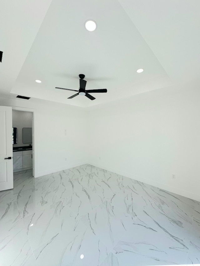 empty room with ceiling fan and a tray ceiling