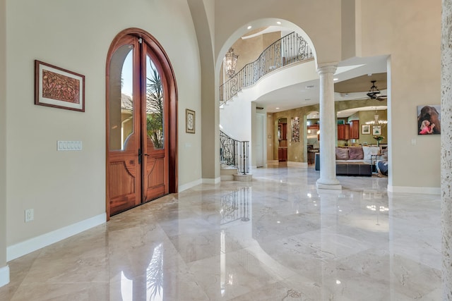 entryway with ceiling fan with notable chandelier, ornate columns, and a high ceiling