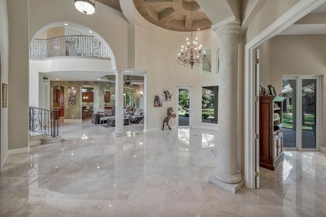 foyer featuring ceiling fan with notable chandelier, a towering ceiling, and decorative columns