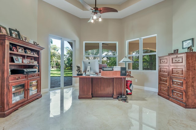 office space with a high ceiling, a raised ceiling, and ceiling fan