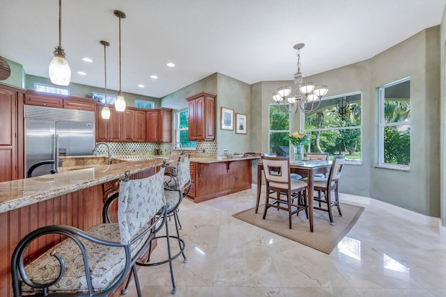 kitchen featuring a notable chandelier, stainless steel built in fridge, light stone counters, and tasteful backsplash