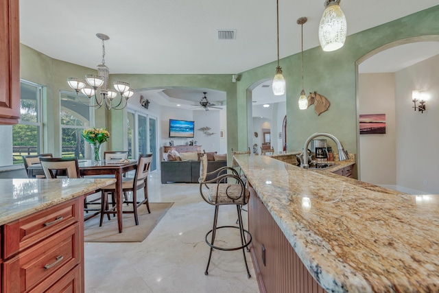 kitchen featuring light stone countertops, a breakfast bar, ceiling fan with notable chandelier, sink, and pendant lighting