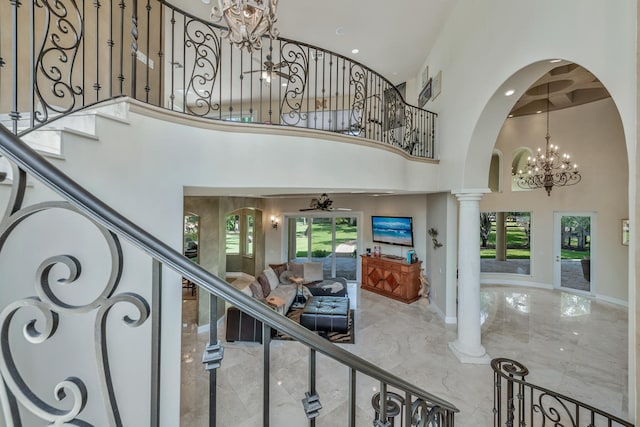 foyer with ceiling fan with notable chandelier, a healthy amount of sunlight, a high ceiling, and decorative columns