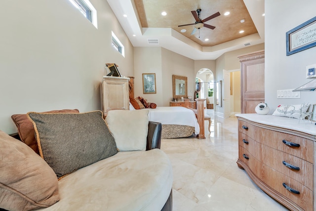 bedroom featuring a tray ceiling, multiple windows, ceiling fan, and a towering ceiling