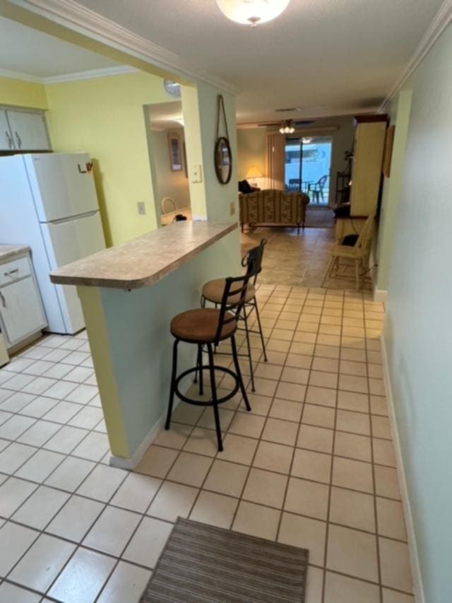 kitchen with a kitchen bar, white fridge, light tile patterned floors, and ornamental molding