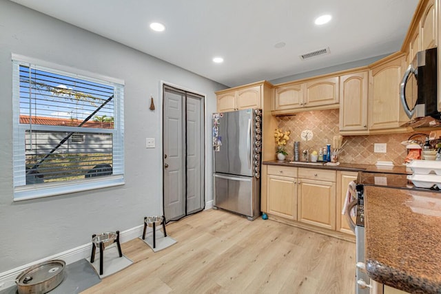 kitchen with light brown cabinets, dark stone counters, decorative backsplash, light wood-type flooring, and appliances with stainless steel finishes