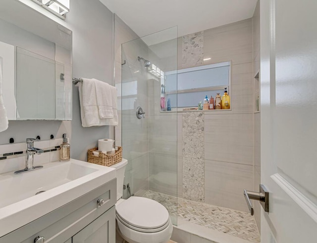 bathroom featuring a tile shower, vanity, and toilet