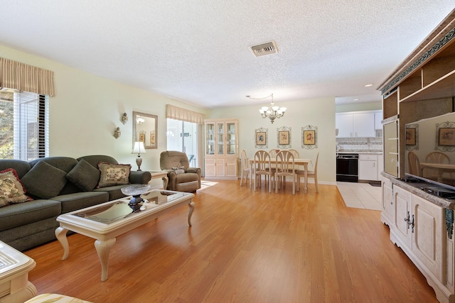 living room with a textured ceiling, light wood-type flooring, an inviting chandelier, and a wealth of natural light