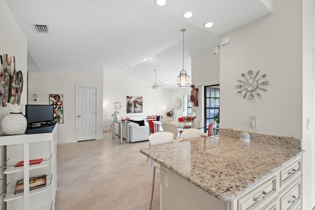 kitchen featuring ceiling fan, light stone counters, vaulted ceiling, decorative light fixtures, and a kitchen bar