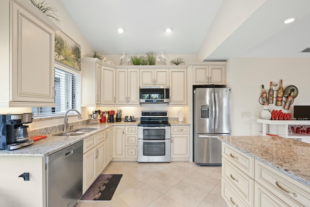 kitchen with cream cabinetry, sink, appliances with stainless steel finishes, and vaulted ceiling