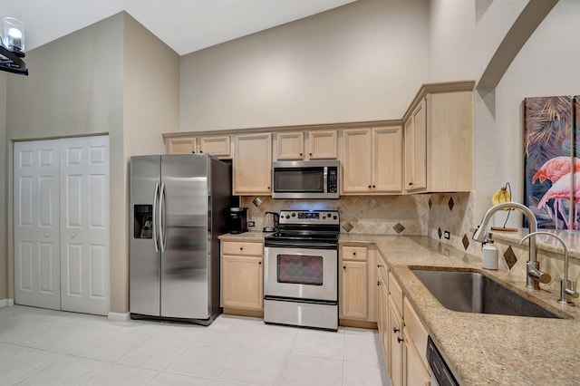 kitchen featuring high vaulted ceiling, sink, light brown cabinetry, light stone counters, and stainless steel appliances